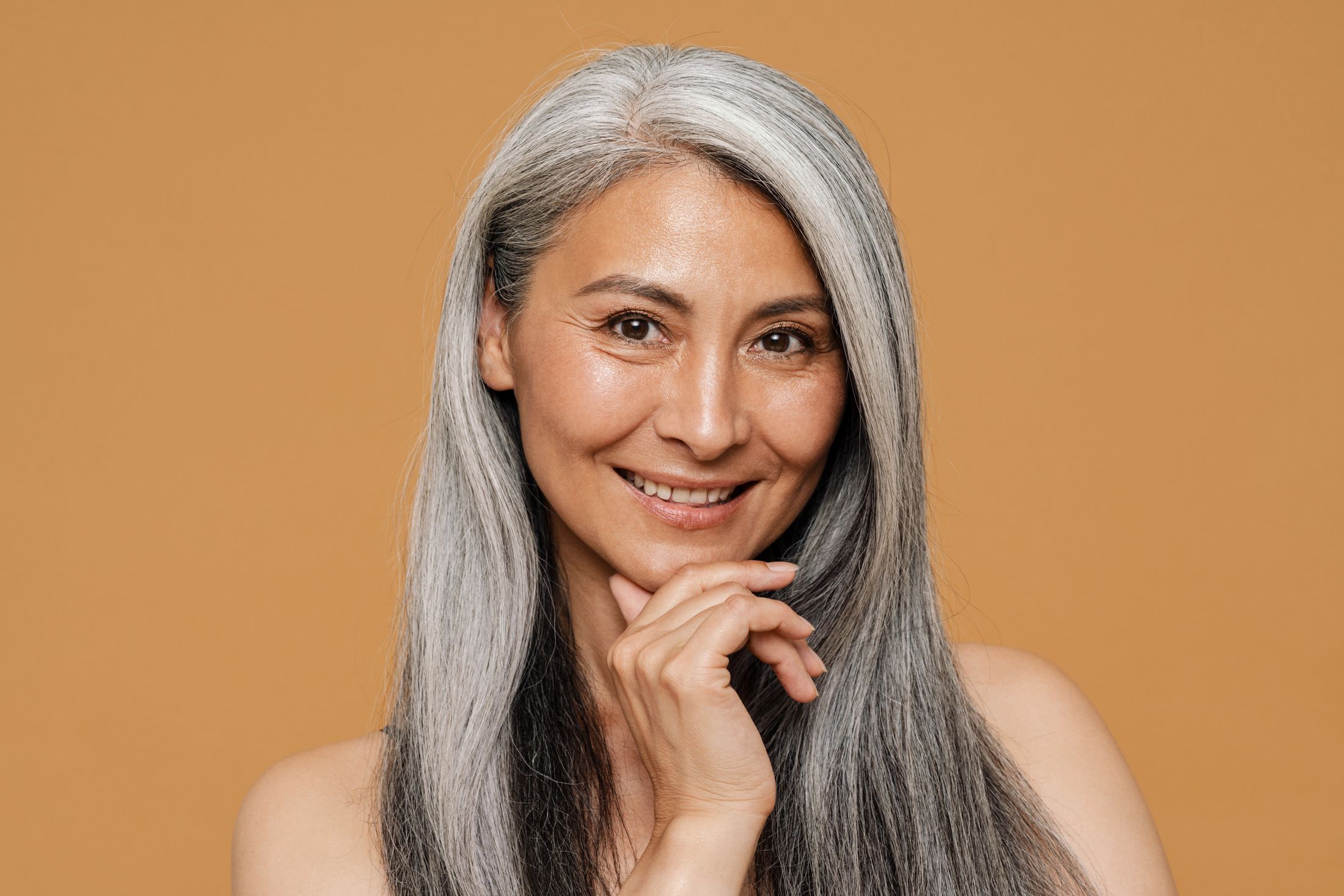 Smiling woman with long gray hair, warm background.